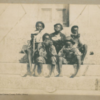 Five African-American boys sitting on granite steps eating watermelons.