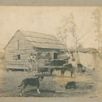 Log cabin with African-American family in ox-cart with two dogs.